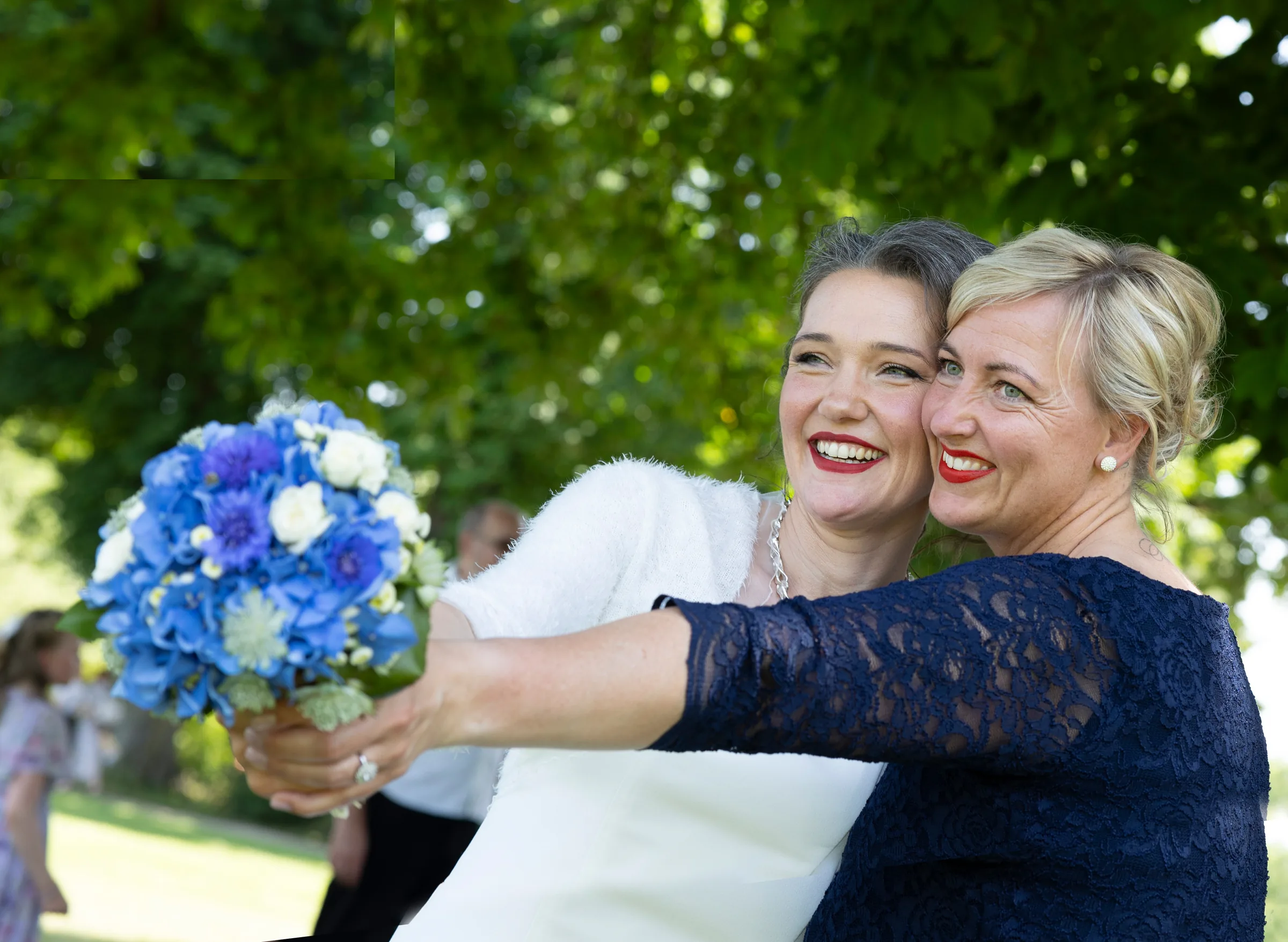 Braut und Trauzeugin mit blauem Brautstrauß im Grünen